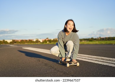 Freedom and happiness. Happy asian girl riding her longboard on an empty sunny road, laughing and smiling, skateboarding. - Shutterstock ID 2239667537
