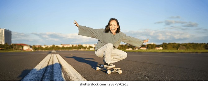 Freedom and happiness. Happy asian girl riding her longboard on an empty sunny road, laughing and smiling, skateboarding. - Powered by Shutterstock