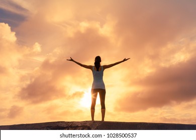 Freedom And Happiness. Woman Standing In The Sunset Reaching Her Arms Up Into The Sky. 