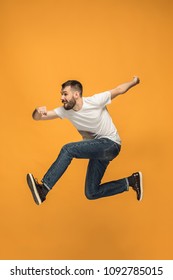 Freedom in moving. Mid-air shot of handsome happy young man jumping and gesturing against orange studio background. Runnin guy in motion or movement. Human emotions and facial expressions concept - Shutterstock ID 1092785015