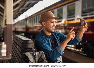 Freedom traveler young asian man at train station taking photo by smartphone. Happy tourist travel by train on vacation time holiday weekend trip. Backpacker arrival at platform railway. - Powered by Shutterstock