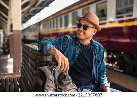 Freedom traveler young asian man at terminal train station. Happy tourist travel by train on vacation time holiday weekend trip. Male Backpacker arrival at platform railway.