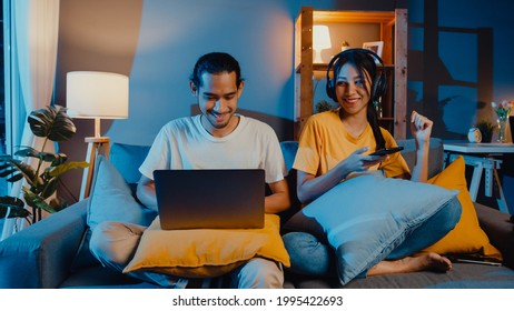 Freelance Asia Couple Man And Woman In Casual Hasband Work  Laptop Computer At Night Enjoy Happy Relax With Wife Wear Headphone Listen Music In Smartphone Sing Dance On Couch At House, Married Life.