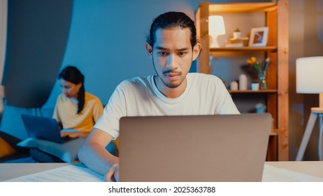 Freelance Asia Couple Man And Woman In Casual Feel Serious Focus On Work Separate Laptop Computer At Night, Hasband Sit In Front On Table Wife Sit Behind On Couch At House. Work From Home Concept.