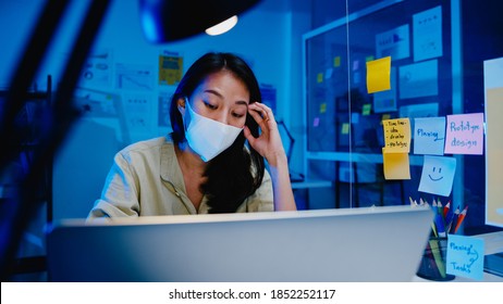 Freelance Asia Women Wear Face Mask Using Laptop Hard Work At New Normal Office. Working From Home Overload At Night, Self Isolation, Social Distancing, Quarantine For Corona Virus Prevention.