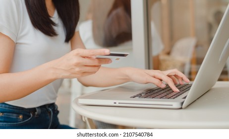 Freelance Asian Women Online Shopping At Coffee Shop. Young Asia Girl Using Laptop, Credit Card Buy And Purchase E-commerce On Internet On Table At An Outdoor Cafe In Evening Concept.