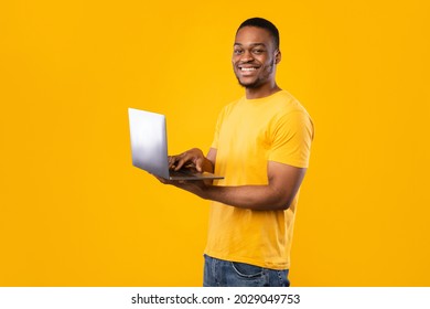 Freelance Career. Happy Black Guy Using Laptop Computer Smiling To Camera Standing Over Yellow Background, Studio Shot. People And Gadgets, E-Learning And Internet Technologies Concept - Shutterstock ID 2029049753