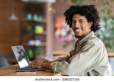 Freelance Career. Happy Young Black Man Working Remotely With Laptop At Cafe, Millennial African American Freelancer Guy Typing On Computer And Smiling At Camera, Enjoying Distance Job Opportunities