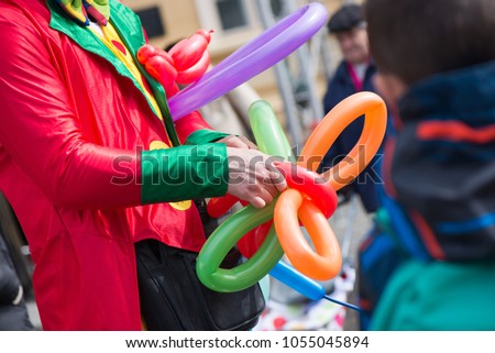 A freelance clown creating balloon animals and different shapes at outdoor festival in city centre. School bag, angel wings, butterflies and dogs made of balloons. Concept of entertainment, birthdays