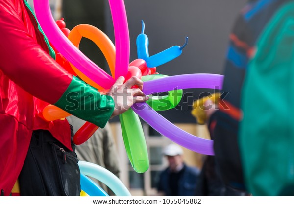 A freelance clown creating balloon animals and\
different shapes at outdoor festival in city centre. School bag,\
angel wings, butterflies and dogs made of balloons. Concept of\
entertainment, birthdays