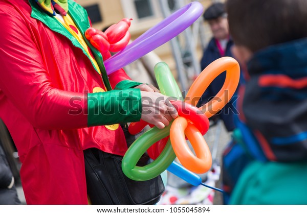 A freelance clown creating balloon animals and\
different shapes at outdoor festival in city centre. School bag,\
angel wings, butterflies and dogs made of balloons. Concept of\
entertainment, birthdays