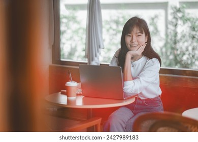 Freelance concept, A delighted young woman smiles at the camera, enjoying her time working on a laptop in a sunlit café corner.