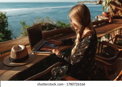 Freelance concept. Pretty young woman using laptop in cafe on tropical beach. Woman freelancer sitting with laptop, amazing sea view