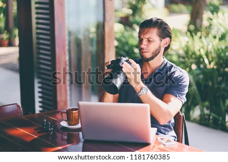 Freelance concept. Professional photographer. Young  bearded man using laptop while sitting on summer terrace.
