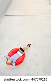 Freelance Concept. Top View Of Relaxed Young Man Working On Laptop Sitting On The Red Bean Bag.