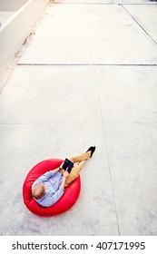 Freelance Concept. Top View Of Young Man Working On Tablet Computer Sitting On The Red Bean Bag.