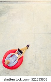 Freelance Concept. Top View Of Young Man Working On Laptop Sitting On The Red Bean Bag.