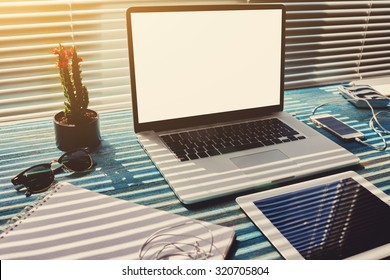 Freelance desktop with accessories and distance work tools, blank screen laptop computer and digital tablet, mouse, sunglasses, phone charging and touch pad, business workspace in home or office