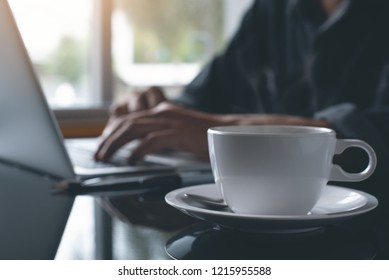 Freelance Man Working On Laptop Computer With Cup Of Coffee On Desk At Coffee Shop Or Home Office With Morning Sunlight, Close Up. Portable Office, Online Working Concept.