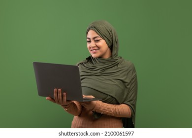 Freelance And Online Education For Muslim Women Concept. Happy Young Lady In Hijab Holding And Typing On Laptop Over Dark Green Studio Background, Copy Space