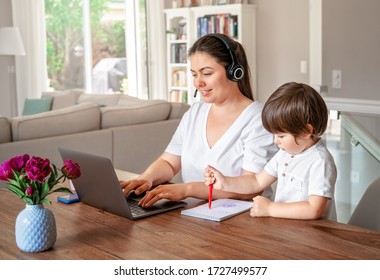 Freelance, online work, studying, learning with child concept. Home office. Woman with headphones working remotely on laptop while her little son drawing next to her.  - Powered by Shutterstock