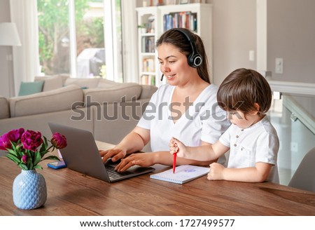 Freelance, online work, studying, learning with child concept. Home office. Woman with headphones working remotely on laptop while her little son drawing next to her. 