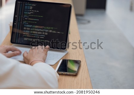 A freelance programmer works remotely, a young woman sits at a table in a coworking or business center and works at a laptop, computer screen and hands on the keyboard close-up