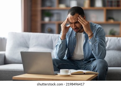 Freelance Stress. Tired Black Guy Looking At Laptop Screen And Rubbing Temples, Stressed African American Male Freelancer Suffering Headache And Lack Of Inspiration While Sitting On Couch At Home