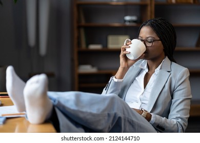 Freelance work-life balance. Calm african american woman freelancer drinking cofee at remote workplace, female office worker relaxing with feet on desk and cup of tea, benefits of working from home