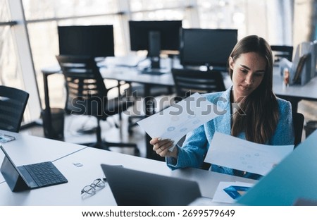 Freelancer analyzes documents with subtle smile, expressing confident ownership, tech-supported clarity and self-assured decision-making in professional role