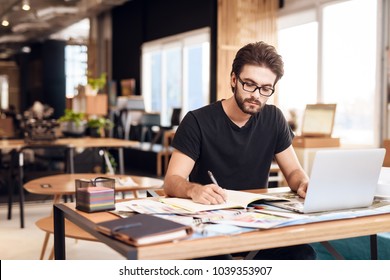 Freelancer bearded man in t-shirt taking notes at laptop sitting at desk. - Shutterstock ID 1039353907