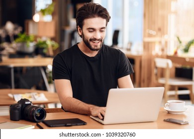 Freelancer Bearded Man In T-shirt Typing At Laptop Sitting At Desk.