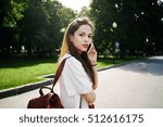 A freelancer is calling to a client by a mobile phone to make an appointment. Young brunette woman is holding a smart-phone while having rest in a city park.