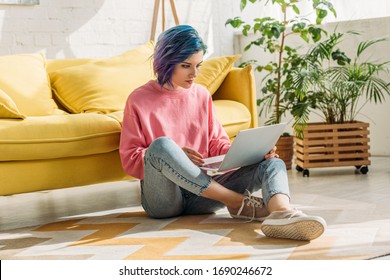 Freelancer With Colorful Hair Working With Laptop Near Sofa In Living Room