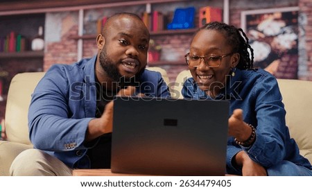 Freelancer couple doing research by reading articles and data driven papers at home, collecting information for a new project. People multitasking and studying online reports on sofa. Camera B.