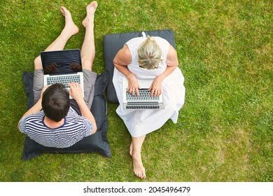 Freelancer Couple Working On Laptop Computer On The Lawn In The Garden In Summer