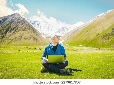 Freelancer digital nomad sit work online type on laptop with mountains scenic panorama.Location independent traveler blogging on travels. Ideas and work online in post pandemic world.Earth day concept