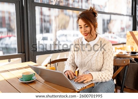 Freelancer enjoying breakfast while working remotely in a cafe, using laptop with city view in the background
