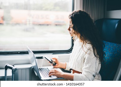 Freelancer girl working and laptop in the train  Girl looking to the phone in her hand  Business travel technology concept 