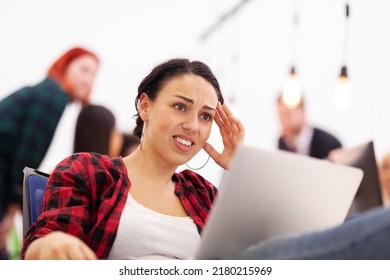 Freelancer Girl Working On A Laptop In A Modern Coworking Office Space. Unhappy Dissapointed Angry Face Expressions. Business Colleagues In The Backgorund