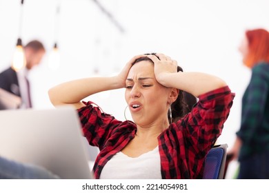 Freelancer Girl Working On A Laptop In A Modern Coworking Office Space. Unhappy Dissapointed Angry Face Expressions. Business Colleagues In The Backgorund