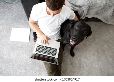 Freelancer Guy With Laptop And Dog Is Working At Home In Quarantine To Coronavirus Infection