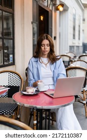 Freelancer Holding Coffee Cup Near Dessert And Laptop On Table Of Cafe In Paris