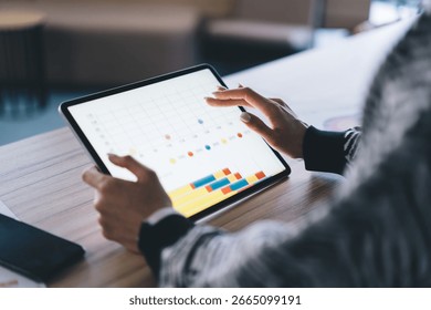 Freelancer interacts with interactive chart on digital tablet, showing multitool control, analytical thinking and smooth integration of modern technology in business process.