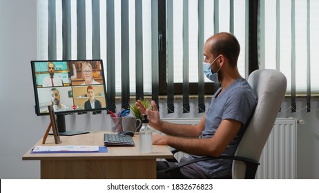 Freelancer Making A Video Conference With Face Mask In Modern Office Room. Entrepreneur Working In New Normal Workplace Having Online Meeting, Webinar With Remotely Team Using Internet Technology