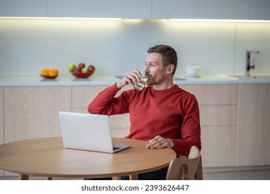 Freelancer man drinking water having break in work sitting at table on kitchen at home with laptop. Freelance, distant remote job concept. Self care, compliance body water balance, healthy habits. - Powered by Shutterstock