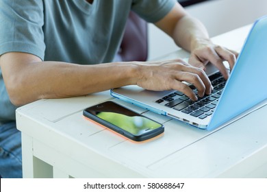 Freelancer man using smartphone buy services on laptop computer in vintage coffee shop. City lifestyle business man hands working on typing keyboard using UI IM IOT IT SEO 4G 5G wifi internet online.