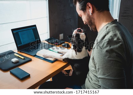 Freelancer man working from home with his dog sitting together in the office.Side view of man using laptop at home with cute dog