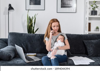 Freelancer Mom Works From Home With A Newborn Baby Girl On Hands. A Working Mother Is Using Laptop While Babysitting At Home, Answering Call On The Phone