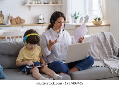 Freelancer mother sit on couch at home office during lockdown, remote work on laptop. Child using tablet, playing in game at tablet, sitting with mom on sofa. Family, telework, e-learning concept.